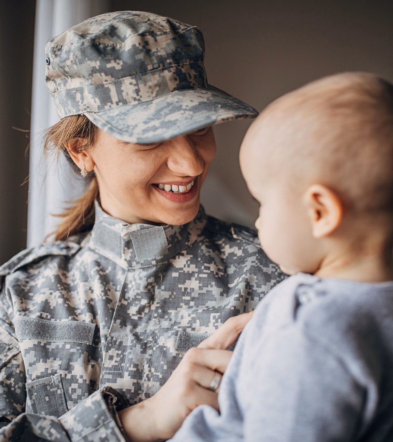 Service member in uniform smiling while holding her infant