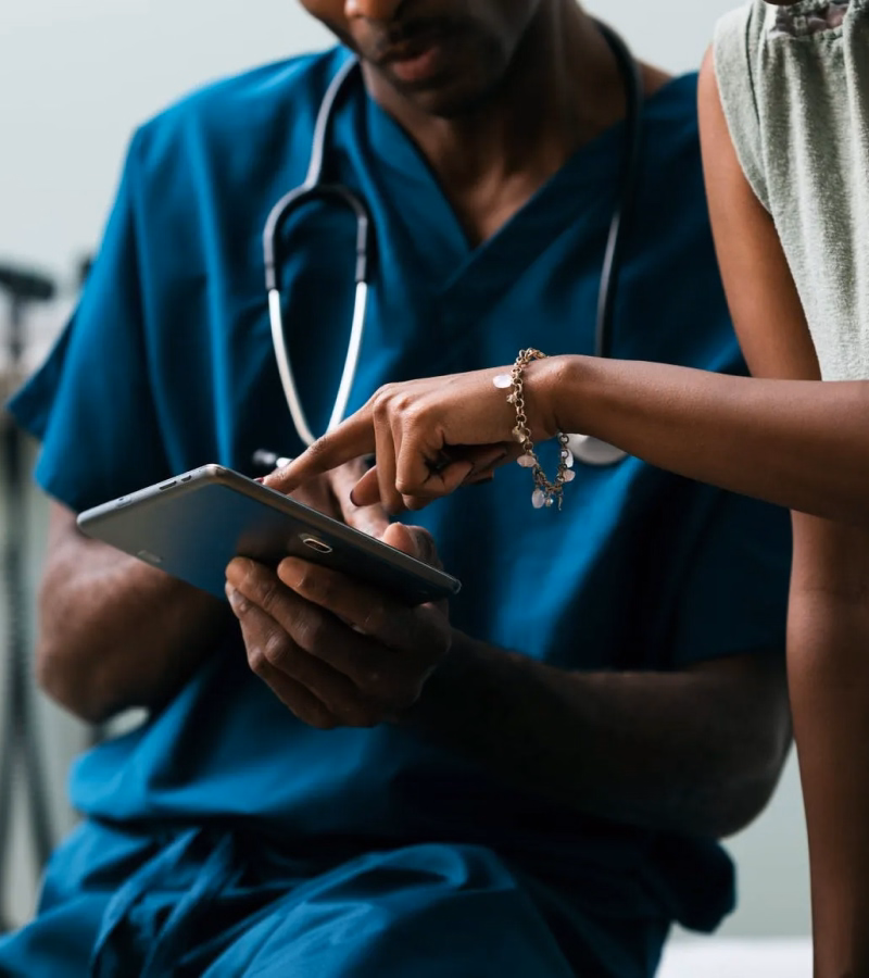 Hospital nurse reviewing patient chart on a tablet at a bedside