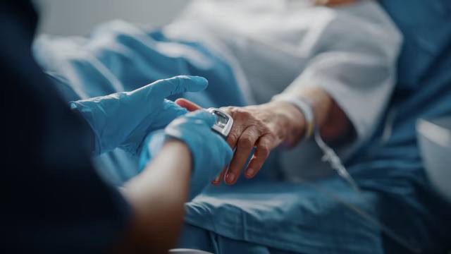 Healthcare worker checking a patient's wrist monitor in a hospital bed