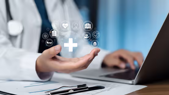 Hand holding a digital healthcare interface with medical icons floating above a laptop