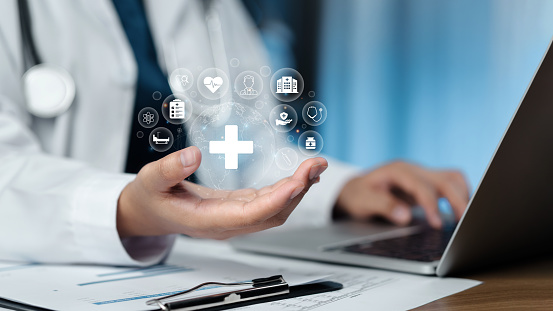 Hand holding a digital healthcare interface with medical icons floating above a laptop